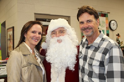 A Santa Claus surrounded by two people, all smiling.